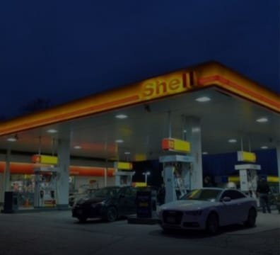 A Shell gas station at night, brightly lit with lights shining on the pumps and surrounding area