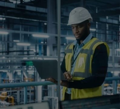engineer in a hard hat and safety vest using a laptop to work on a project