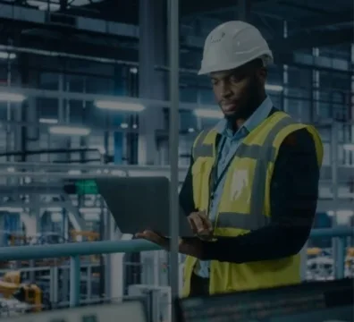 engineer in a hard hat and safety vest using a laptop to work on a project