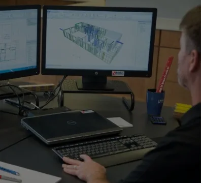 A man sitting at a desk with two computer screens, working on his tasks.
