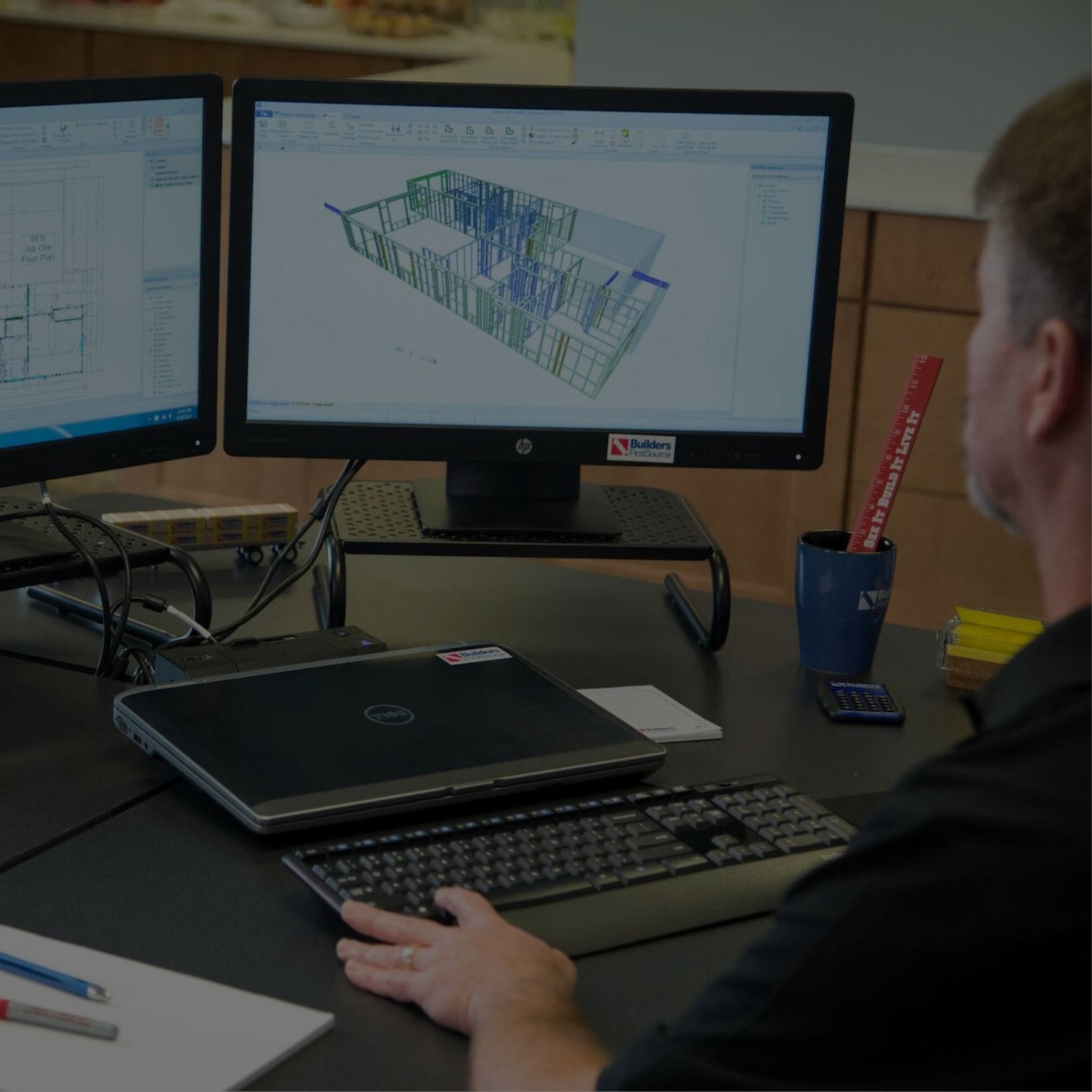 A man sitting at a desk with two computer screens, working on his tasks.