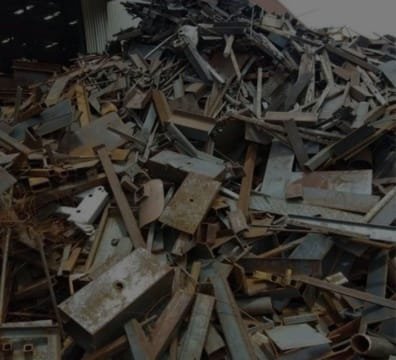 A pile of discarded Iron and Scrap Metal in front of a building.